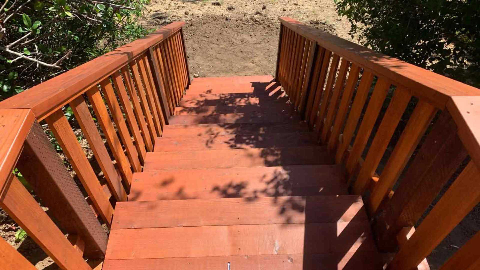 Stained wooden outdoor staircase with railings leading down a slope