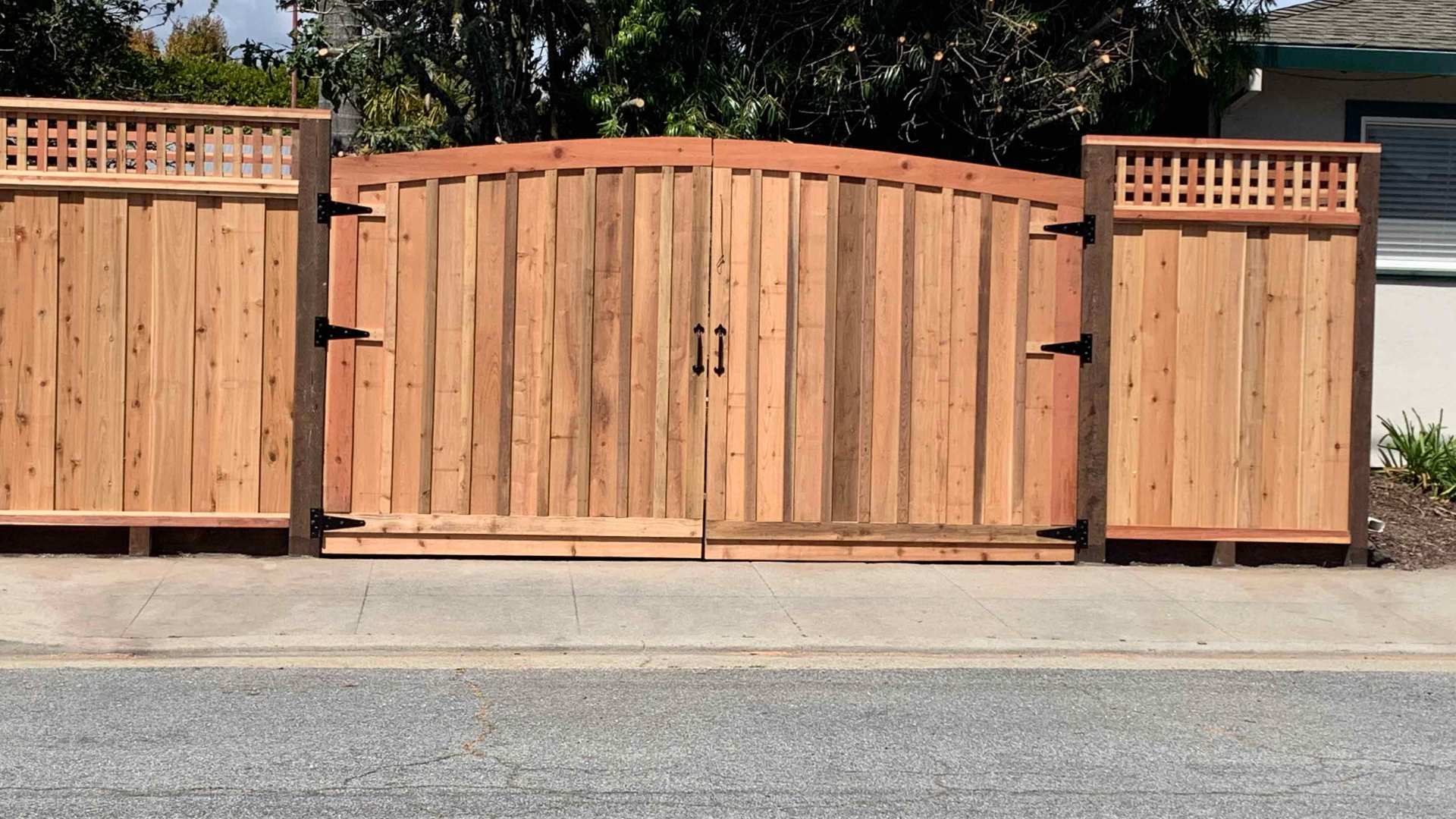 Wood double gate with vertical planks and an arched top, featuring large black hinges.