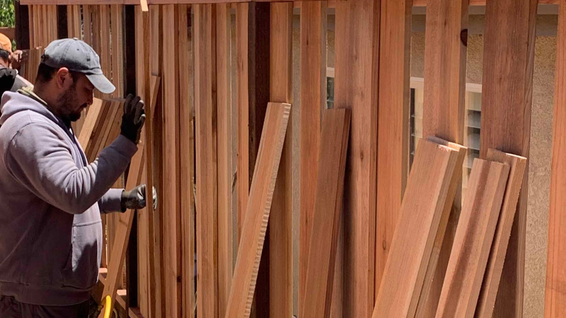 Worker installing vertical wooden boards for a new fence construction