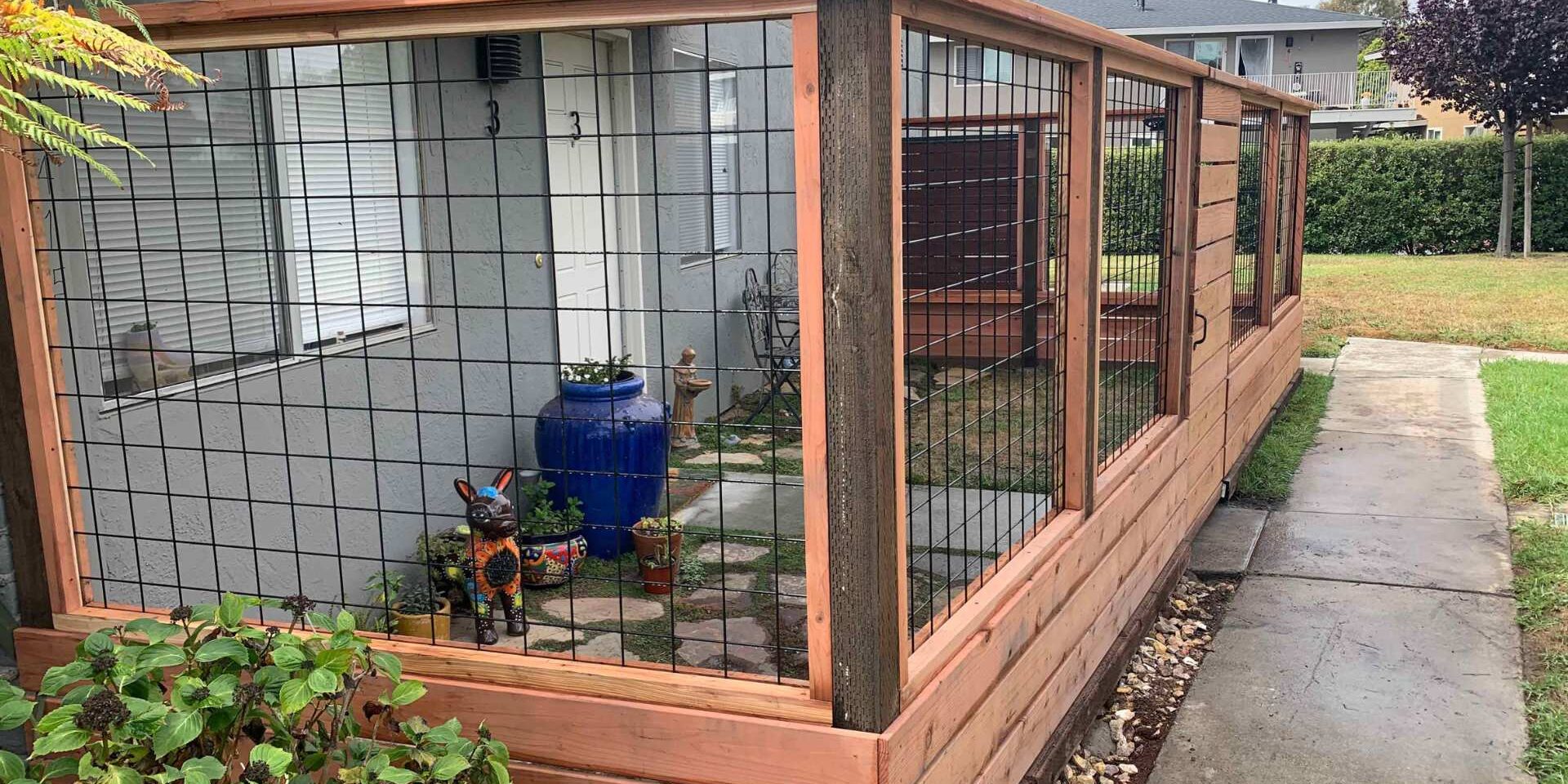 Wood fence with horizontal planks on the bottom and black wire mesh panels on the top, enclosing a small patio area with a blue vase.